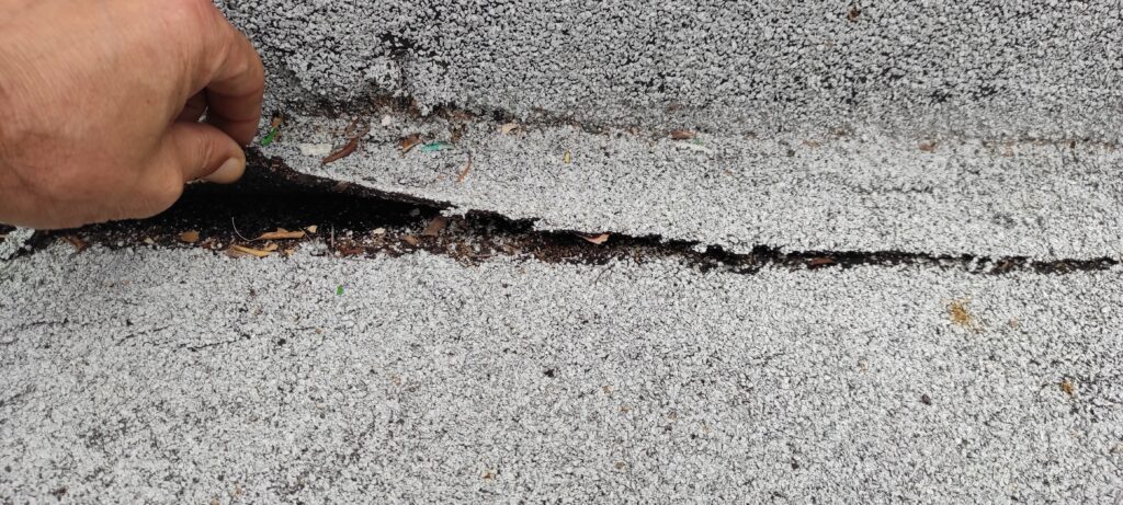 Main décollant le relevé de flashing sur une toiture terrasse, soulignant un défaut d’étanchéité à corriger