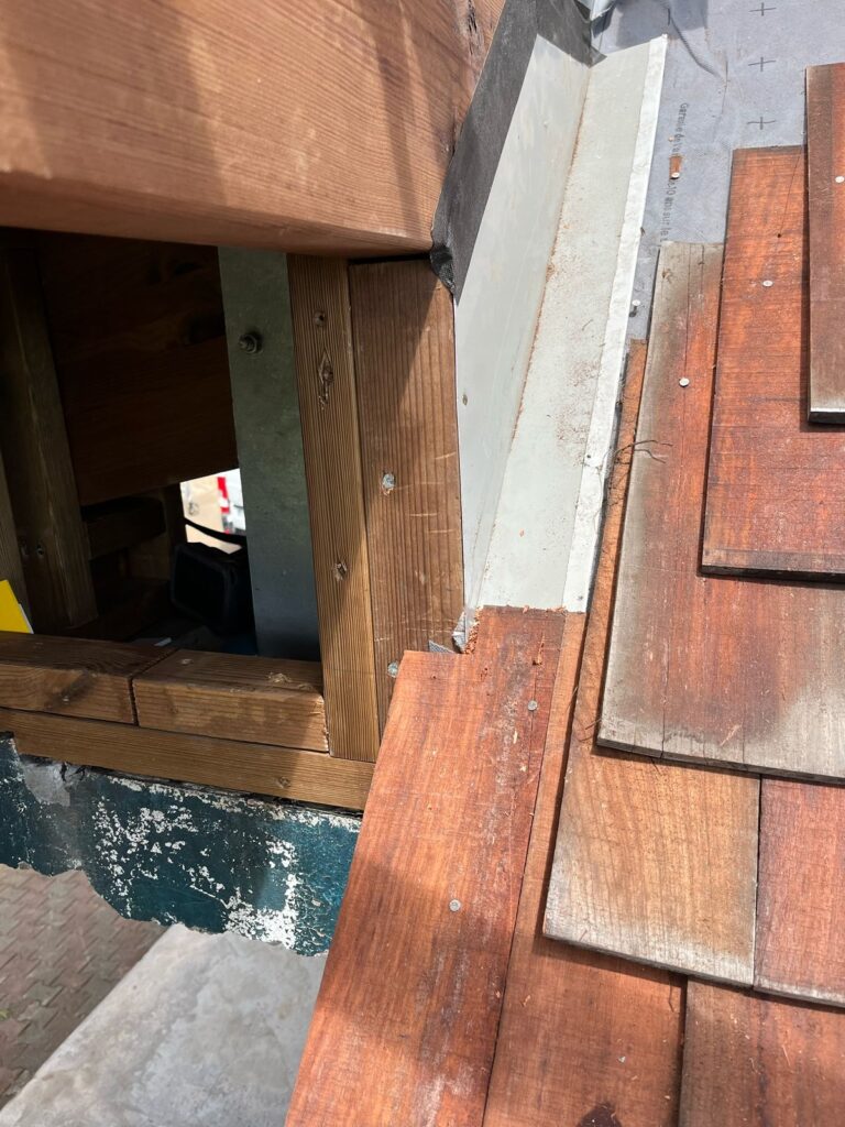 Raccord de couverture en bardeau bois à La Réunion avec recouvrement longitudinal non conforme, présentant un risque de fuite.