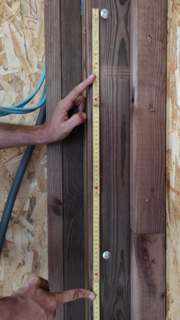 Vérification de la distance entre deux fixations sur un montant vertical d’ossature bois à l’aide d’un mètre pour garantir la précision de l’installation.
